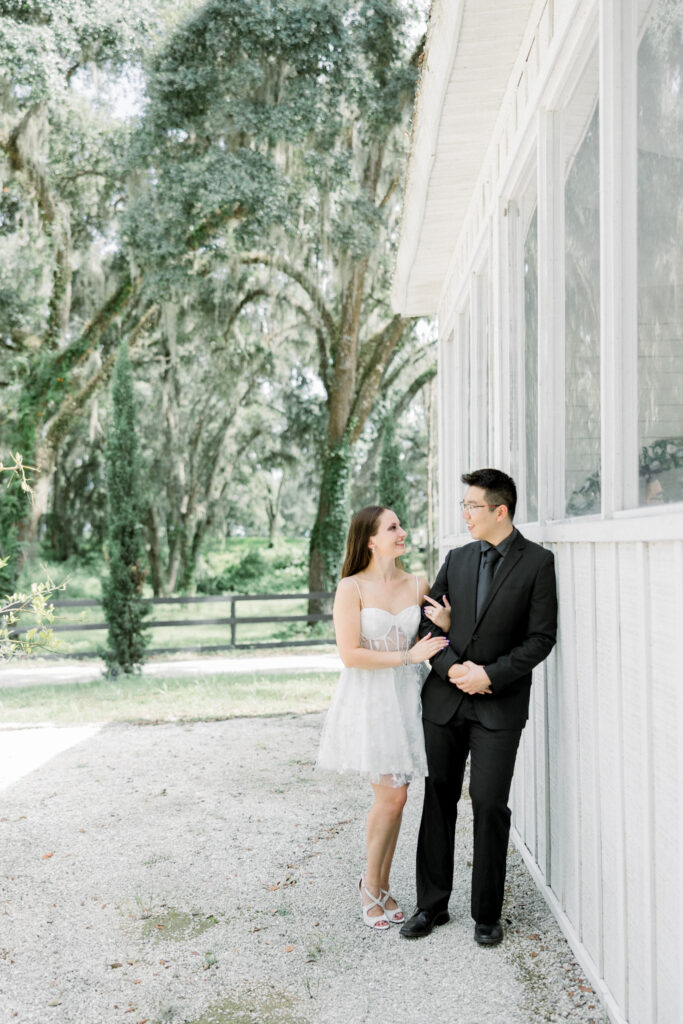 Wide shot of couple embracing in open field with Tuscan-inspired architecture in the background