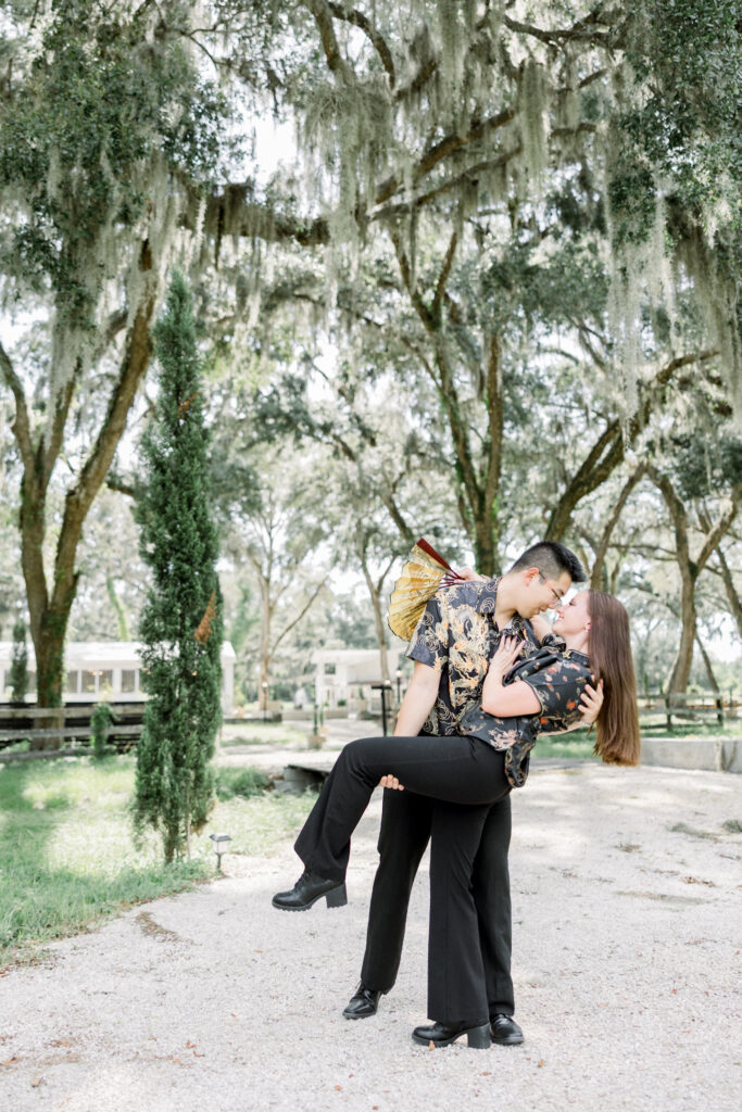 Wide shot of couple embracing in open field with Tuscan-inspired architecture in the background