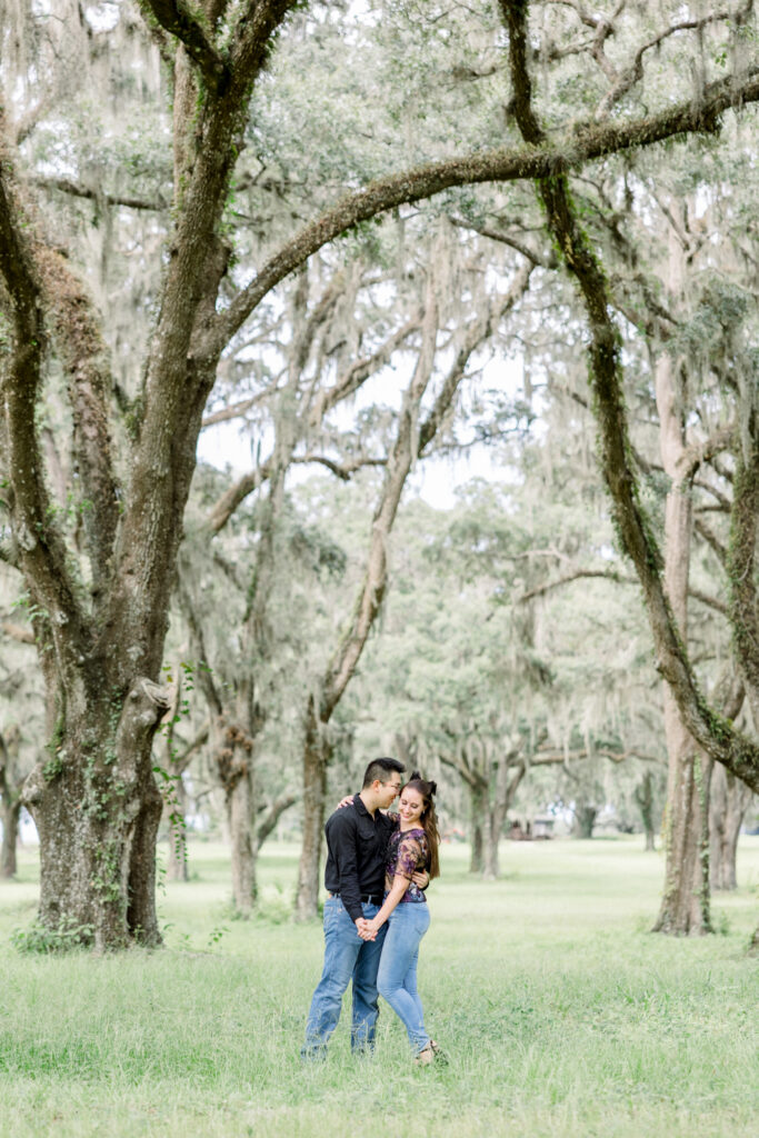 David and Brooke walking hand-in-hand under Spanish oak trees at Andalusian Oaks